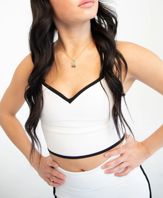 A woman wearing a white crop top with black trim and a matching white bottom, shown from the neck down against a plain white background.